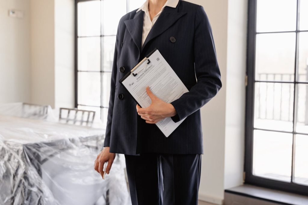 Professional real estate agent holding documents in a sunlit room, symbolizing success and transactions.